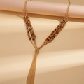 Dettaglio della collana boho a tre strati con nappe e perle di vetro su catene dorate - Marrone