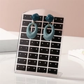 Teal geometric earrings hanging on a black acrylic 72-hole stud display organizer - Transparent + Black Grid