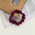 Elegant burgundy satin scrunchie resting on a vintage wallet and printed book pages - Burgundy