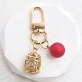 Detail of golden birdcage keychain and matte red sphere charm on geometric stand - Matte Red Pearl + Birdcage