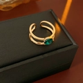 Macro detail of gold-plated crossover ring featuring a pear-cut emerald green gemstone - Gold-Green