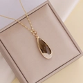 Close-up of golden waterdrop pendant with brown crystal and sparkling pave diamonds - Coffee