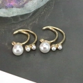 Primer plano de pendientes dorados de doble arco con tres perlas blancas en fondo oscuro - Estilo 5/Pendientes de Perlas Curvos de Doble Capa