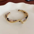 Close-up of golden wavy cuff bracelet with leopard tortoise pattern on ceramic tray - Gold Wave Patchwork Tortoiseshell Style