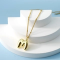 Golden bubble initial M pendant necklace with delicate chain on geometric display - Letter M(M)