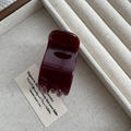 Dettaglio di una molletta per capelli lucida bordeaux su una superficie testurizzata - Caffè Rosso Jelly