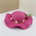 Detail of rose red straw sun hat with wavy brim and delicate pink floral decorations - Rose Red