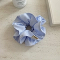 Close-up of blue and white striped fabric scrunchie with detailed stitching and logo tag - Blue Stripe