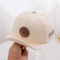 Dettaglio del cappellino neonato in cotone crema con toppa lettera B e visiera morbida - Bianco Sporco / 50cm 1-3 Anni