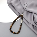 Detailansicht der Tigerauge-Handykette mit weißen Perlen auf grauem Seidenstoff - K3407 Tigerauge Naturstein + Weißer Jade Bodhi Handykette