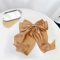 Close-up of a large golden brown satin bow hair clip on a minimalist white table - Champagne