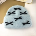 Detailed view of light blue knitted hat with black velvet bows on a gold tray backdrop - Light Blue