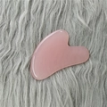 Pink heart-shaped rose quartz gua sha tool for facial massage on grey plush background - Pink Gua Sha Board