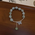 Macro shot of green beaded bracelet with hollow butterfly charm on a wooden base - Green-Butterfly-Vintage