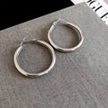 Detail van grote zilveren oorringen met gepolijste spiegelafwerking op grijze textuurstof - Zilver