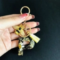 Macro detail of resin letter P keychain with white daisy, gold foil, and bee charm - Letter P