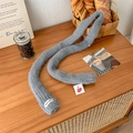 Gray knitted skinny scarf with VEGETABLE label and heart tag on a cozy wooden desk - Gray