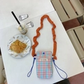 Détail du sac à bandoulière à carreaux avec bandoulière orange plissée sur table - Grille Orange