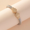 Two-tone stainless steel cable wire cuff bracelet with gold floral ends on a stand - Gold