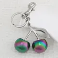 Iridescent cherry keychain with silver metal hook on white waffle texture fabric background - Colorful Cherry with Silver Leaf