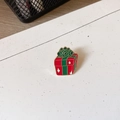 Dettaglio ravvicinato di una spilla smaltata a forma di pacchetto regalo natalizio - Scatola regalo