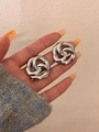 Close-up of knot design silver stud earrings with hollow flower detail on model hand - Silver