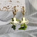 Detailed shot of gold octopus earrings with green stone pendants on stone surface - Octopus