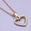Detail of a golden stainless steel necklace featuring a hollow heart-shaped pendant on purple - Pendant with Necklace / Gold