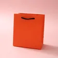 Detailed view of an orange textured paper gift bag with sturdy black woven rope handles - 12x11x6cm / Orange