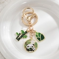 Close-up of panda and bamboo enamel pendants with gold-plated keychain on white plush base - Panda Eating Bamboo