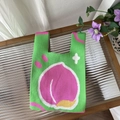 Detailed close-up of green knit tote bag with a pink peach pattern on a glass table - Peach Green