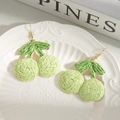 Detalle de pendientes de cereza tejidos a mano en rafia verde sobre plato blanco - Cian