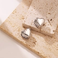 Primer plano de pendientes de corazón en plata pulida sobre piedra con reflejos elegantes - Plateado