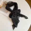 Detail eines schwarz-weiß gepunkteten Seidenschals, als Schleife gebunden auf weißem Tisch - Mit Seidenschal / Schwarzer Polka Dot