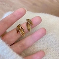 Close-up of golden leaf earrings with amber crystals held against a soft beige knit fabric - Dark Brown