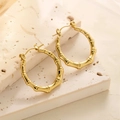 Détail des boucles d'oreilles créoles bambou plaquées or 18k sur une surface en pierre - EH021/Bambou Naturel