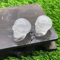 Mini crystal skull carved from transparent clear quartz shown on a rustic dark wood base - White Crystal