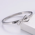 Dettaglio di un bracciale rigido a fiocco argentato con zirconi su supporto di pietra - Color Acciaio
