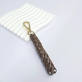 Handmade brown and white braided key charm with golden lobster clasp on minimalist tray - Tan