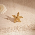 Close-up of golden starfish ear clip with granular texture on a beige stone surface - Clip Earring - Gold Spotted Starfish