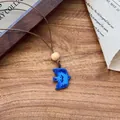 Close-up of a blue ceramic bird pendant with wooden bead on a rustic wooden table - 6# Necklace - Coffee - Royal Blue Bird