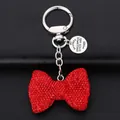 Close-up of red rhinestone bow keychain with vintage metal tag on black leather background - Red