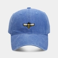 Close-up of detailed yellow and black bee embroidery on a washed blue cotton baseball cap - Light Blue