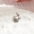 Macro shot of silver metal star pendant with polished finish on white textured surface - Star / Silver