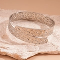 Macro detail of silver open cuff bracelet featuring intricate floral vine engravings - Silver