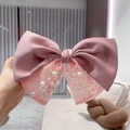 Close-up of pink satin bow hair clip with decorative pearls and elegant fabric texture - Pink