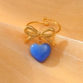 Golden stainless steel bow ring with blue heart pendant shown on sparkling fabric - Light Blue Style