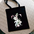 Black canvas tote bag with pink letter T and white lily floral print on woven mat - Letter T / Black