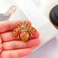 Dettaglio di una spilla ape barocca con smalto arancione, perle e cristalli in mano - Rosso Arancio