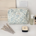 Gesteppte Blumentasche für Kosmetik mit Pinseln und Beauty-Produkten auf Tisch - Blaues Blumenmuster